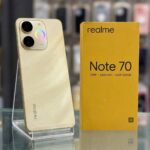 هاتف realme Note 70 باللون الذهبي بجانب علبته الصفراء الأصلية